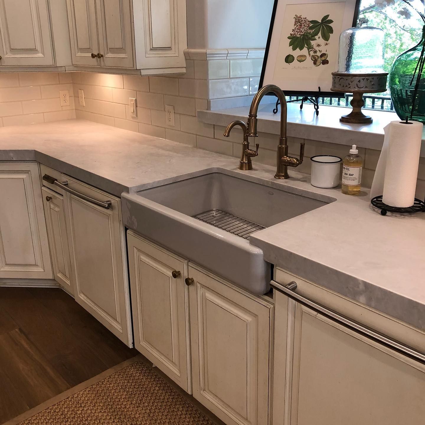 Kitchen with white cabinets, farmhouse sink, gold faucet, and gray countertops.