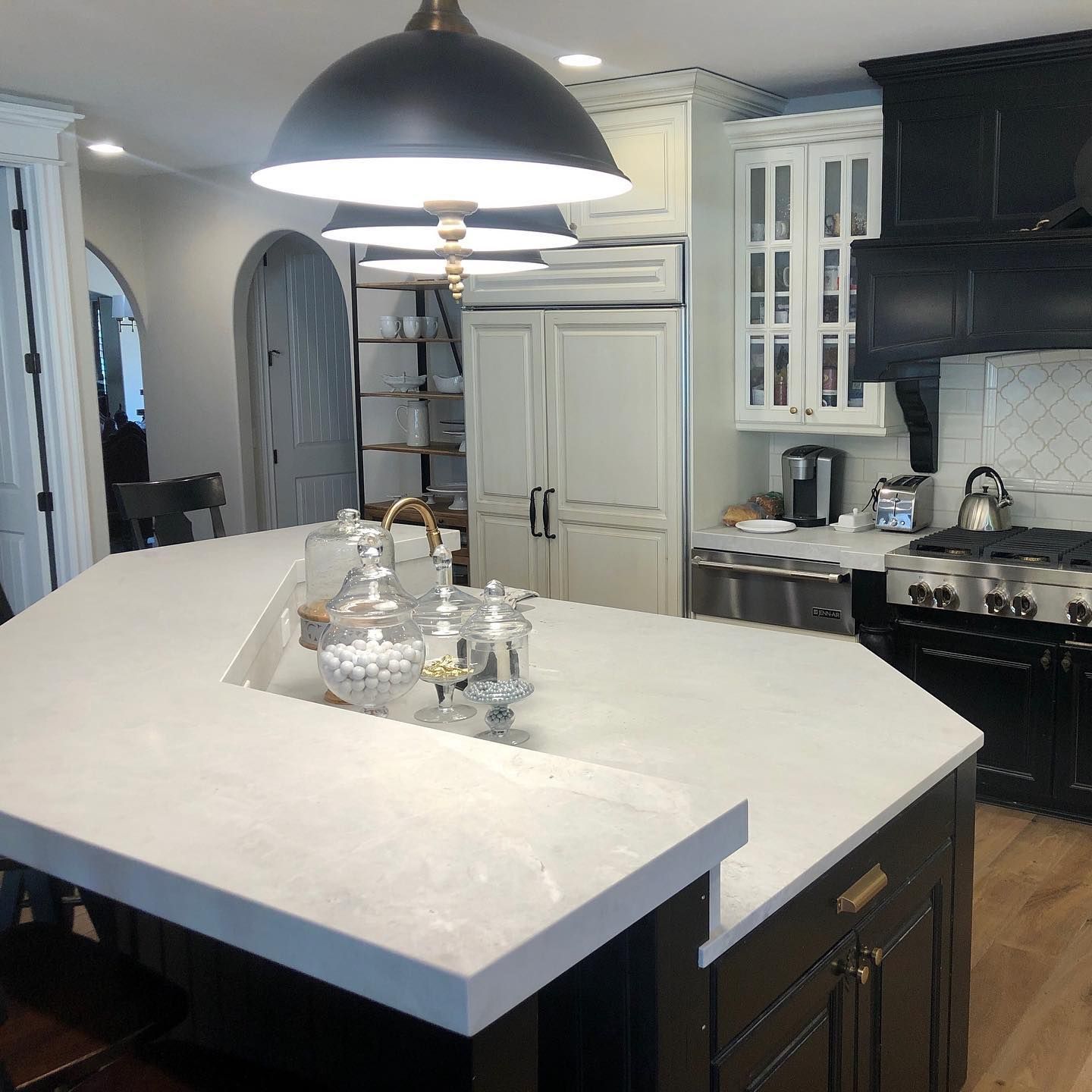 Kitchen with black island, white countertops, black hood, and cream cabinets.