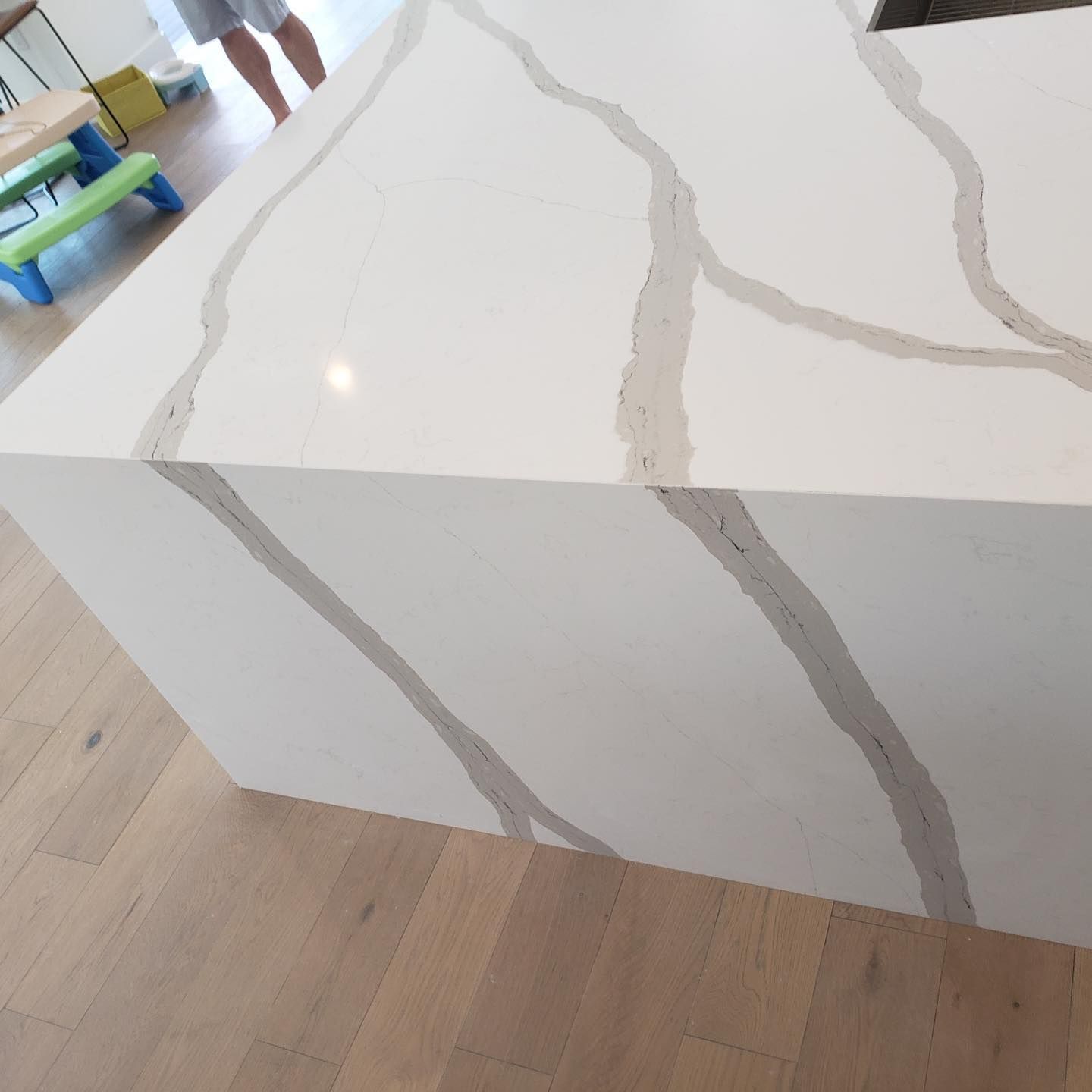 White kitchen island with grey veining, on a light wood floor.