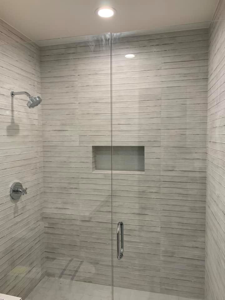 Modern shower with textured white tile walls, glass door and shower head.