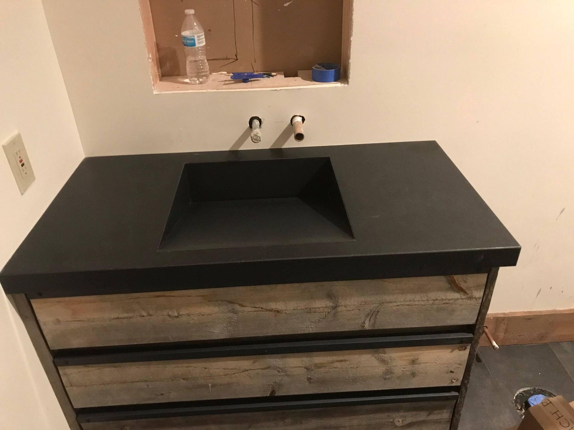 Bathroom vanity with black countertop and wooden drawers. Wall-mounted faucet.