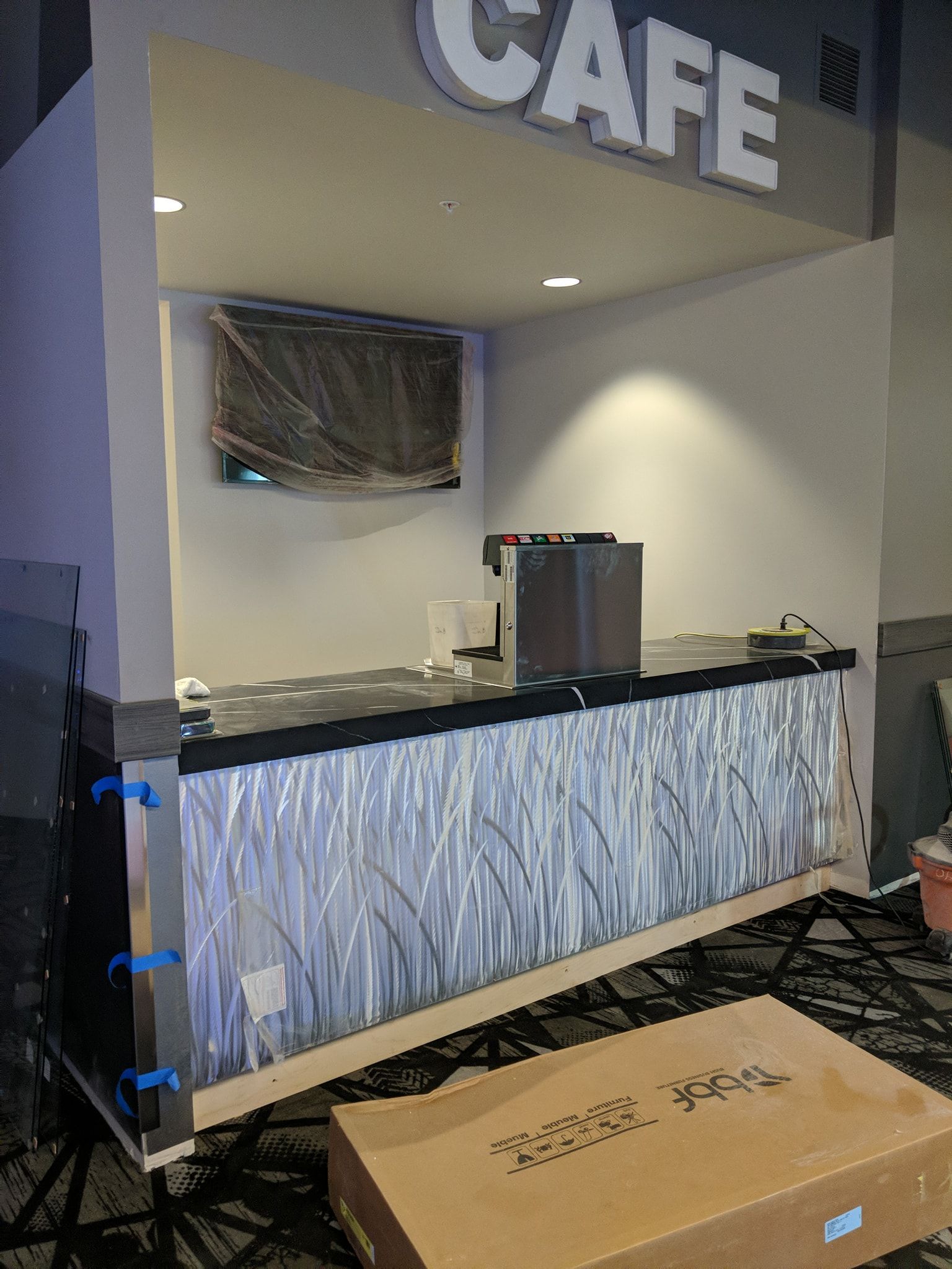 Cafe counter with silver design and sign; a TV is mounted above.