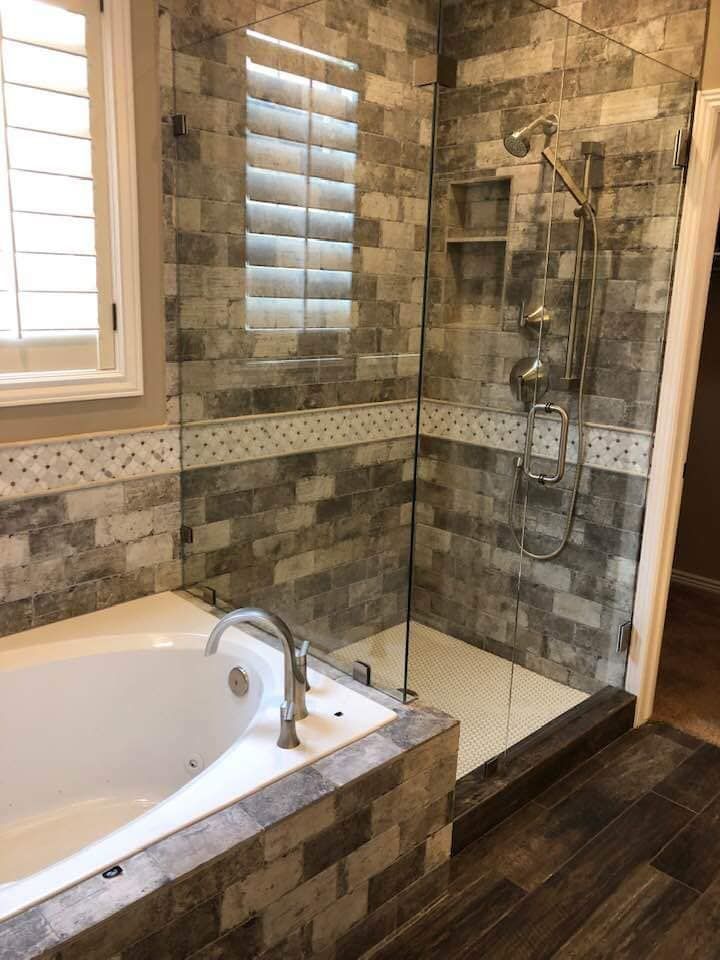 Bathroom with a tub and a glass shower. Gray and white brick tiles and wood floor.