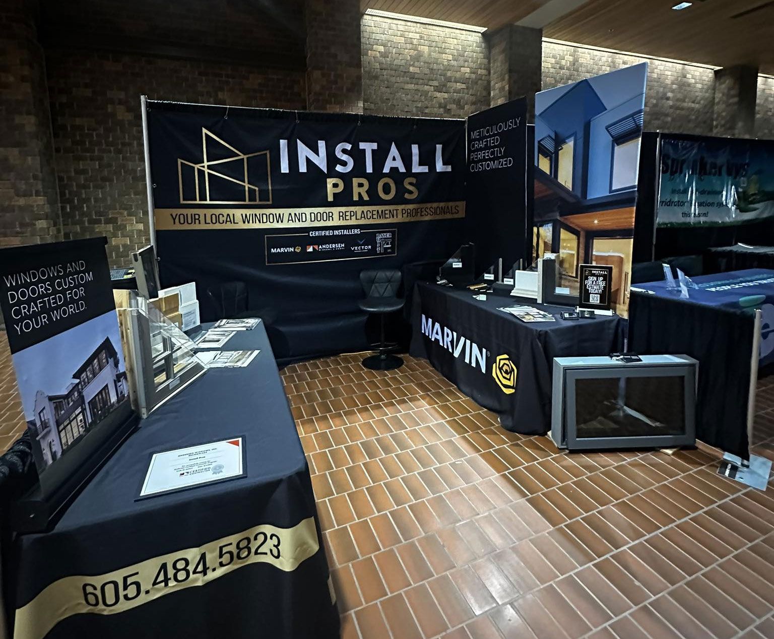 Trade show booth with black tablecloths and banners, showcasing "Install Pros" with their logo and phone number.