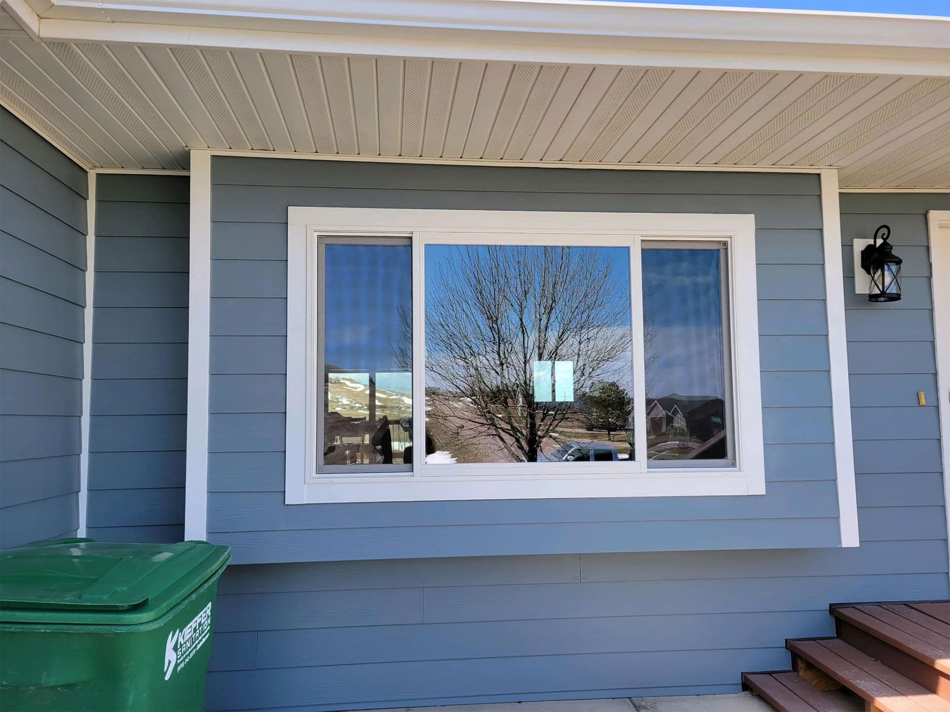 Blue house exterior with a reflective window, trash can, and steps.