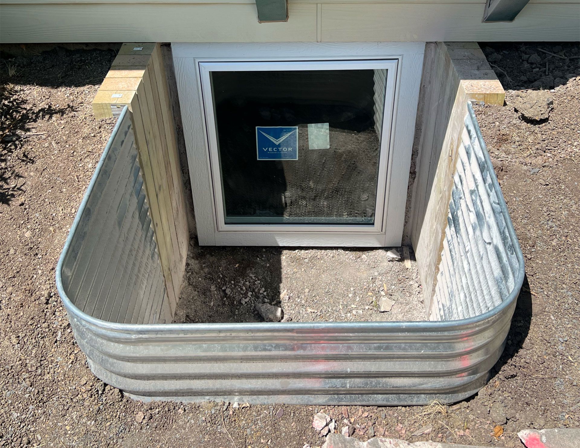 Window well with corrugated metal walls. Light frame window on concrete. Soil.