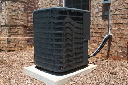 a black air conditioner is sitting on a concrete block in front of a brick building