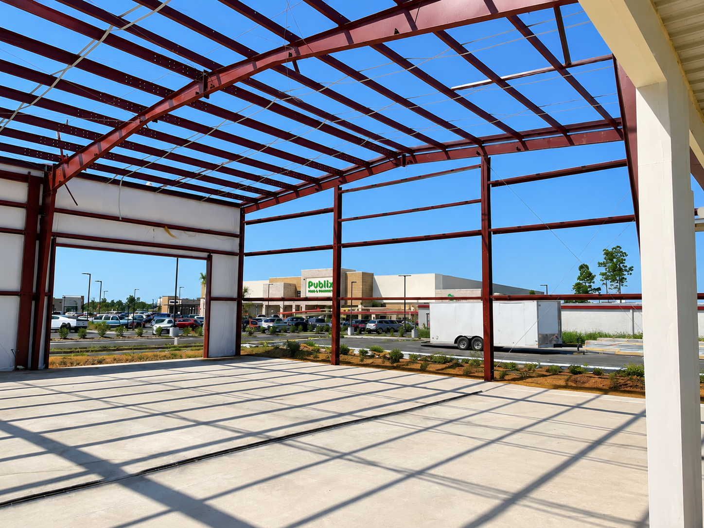 Open steel-framed building under construction with a concrete floor and blue sky overhead