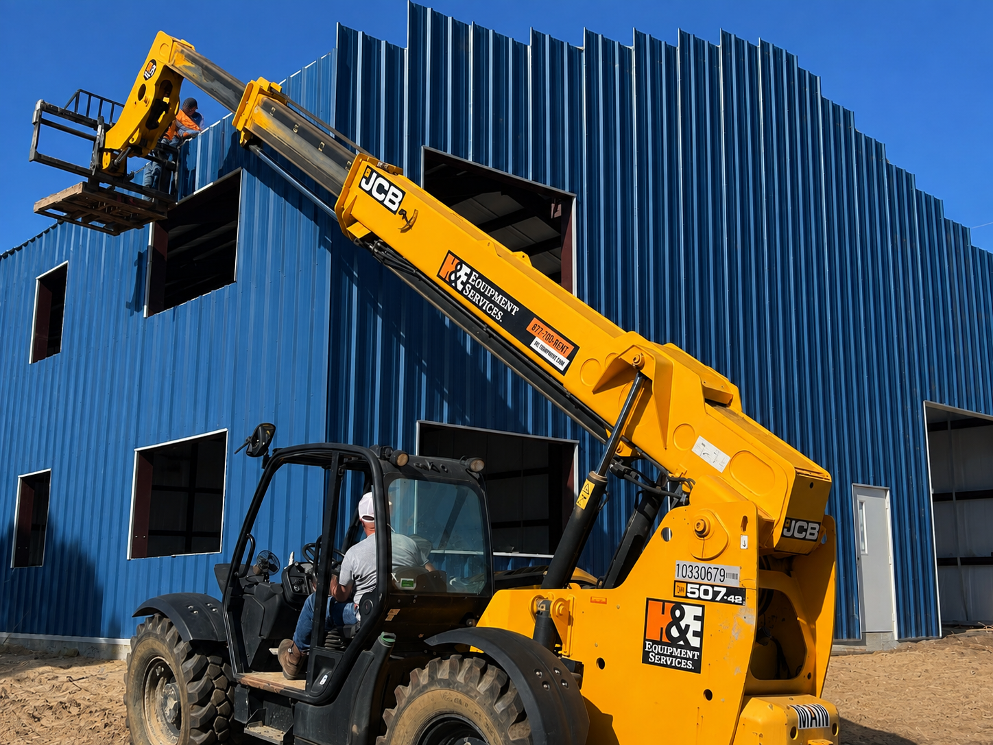 Yellow telehandler lifting materials beside a blue corrugated metal building under construction