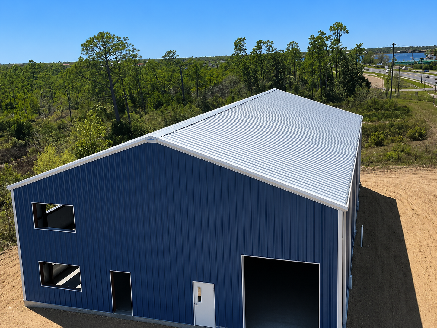 Blue metal barn with white trim, open garage door, and gravel foreground under a bright sky