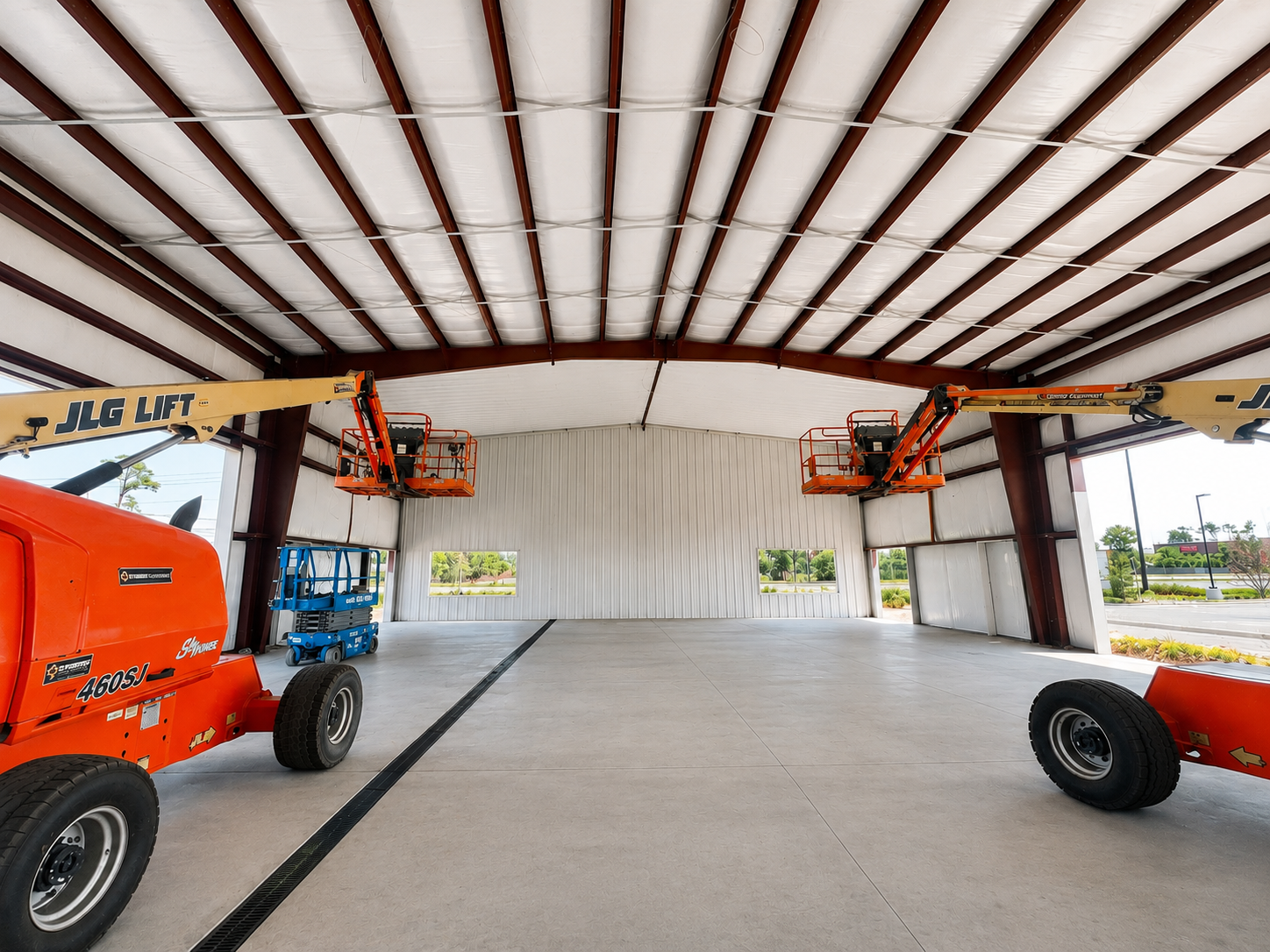 Inside a hangar, orange and blue tractors sit on a concrete floor beneath a metal roof.