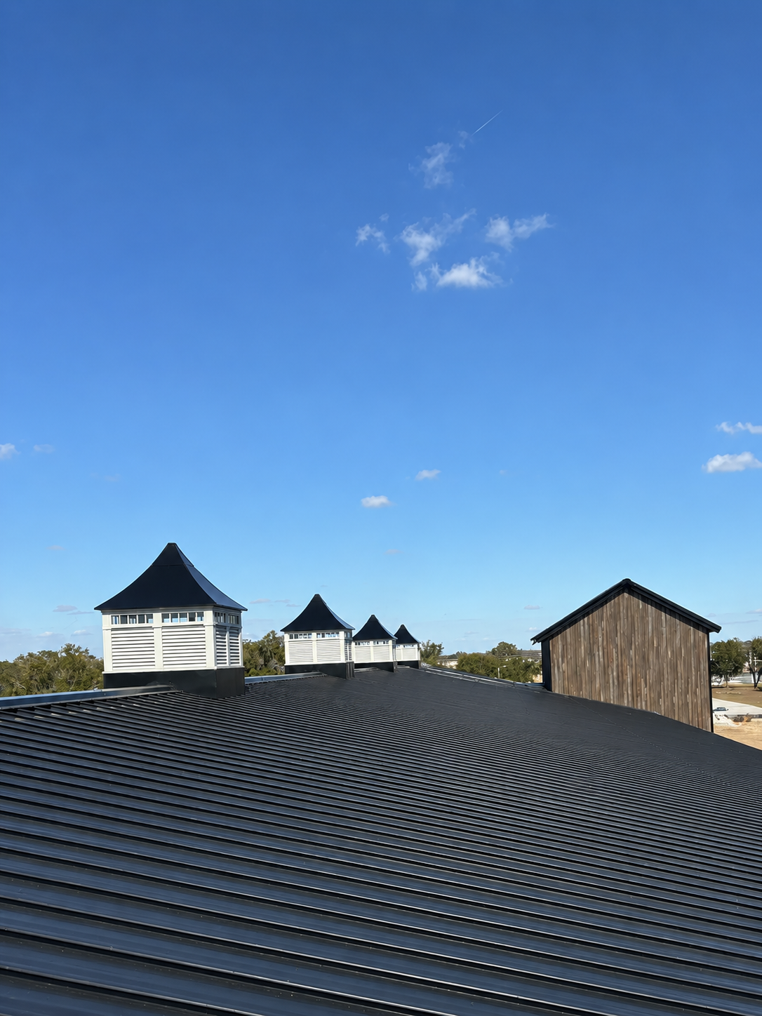 Large rustic building with dark roof beside an open paved lot under a partly cloudy sky