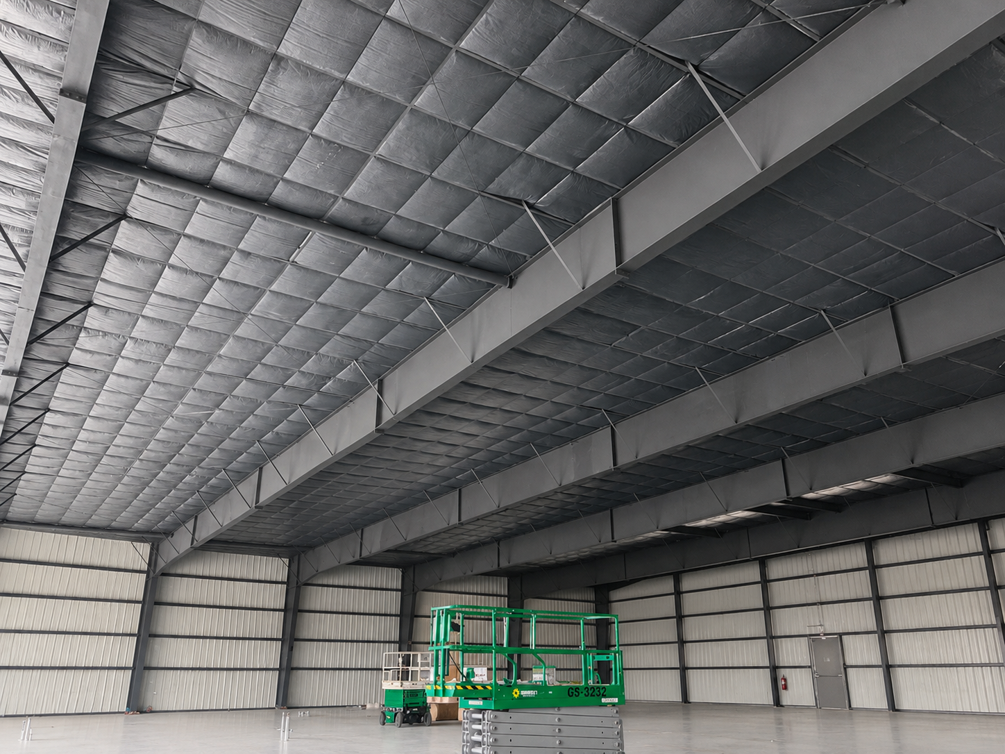 Large empty warehouse interior with insulated metal walls and a green scissor lift near the back.