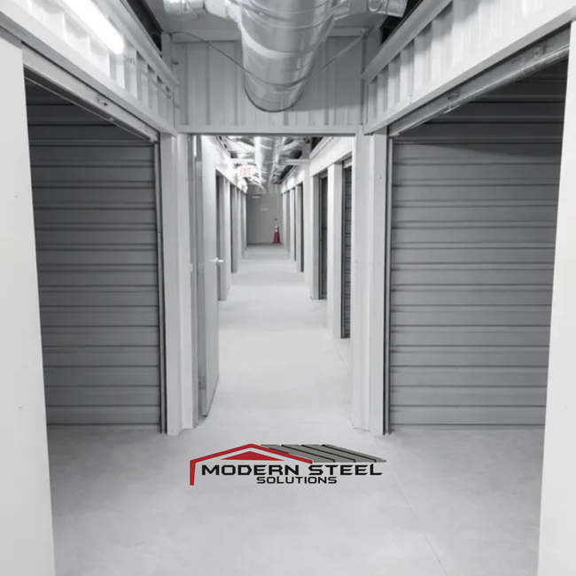 Bright white hallway in a storage facility with rows of gray roll-up doors and exposed overhead ductwork