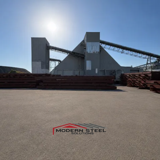 Industrial plant with conveyor belts under a bright sun, viewed from a wide open lot.