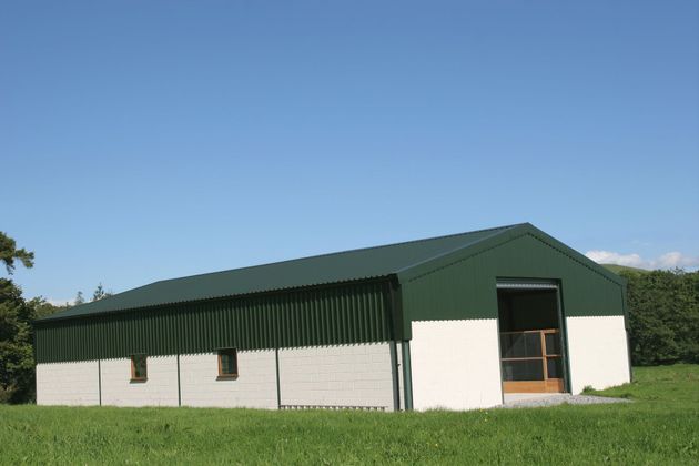 White and green metal barn with sloped roof in a grassy field under a blue sky