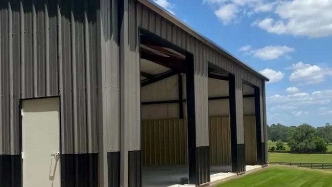 Large metal barn with open bays beside a green field under a blue sky