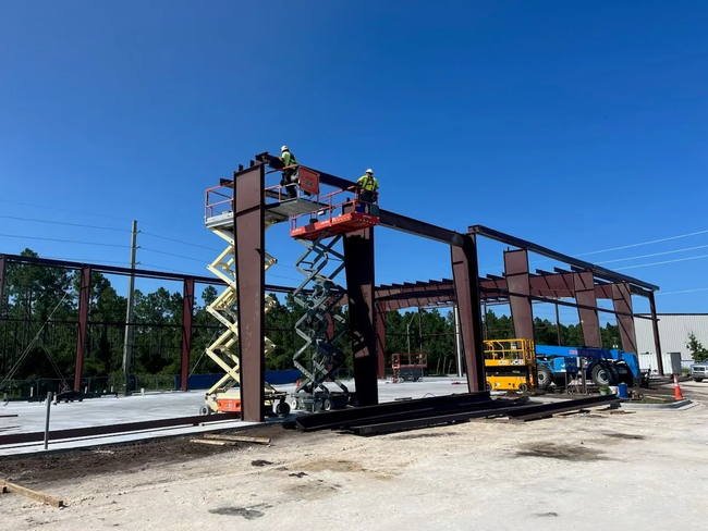 Construction workers on steel frame beams at a building site under a clear blue sky.