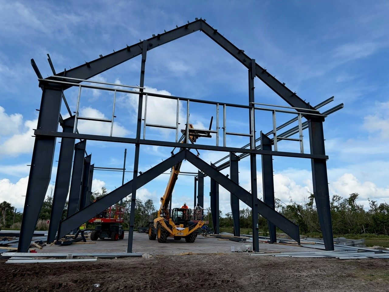Partially built wooden frame structure with workers and equipment under a blue sky.