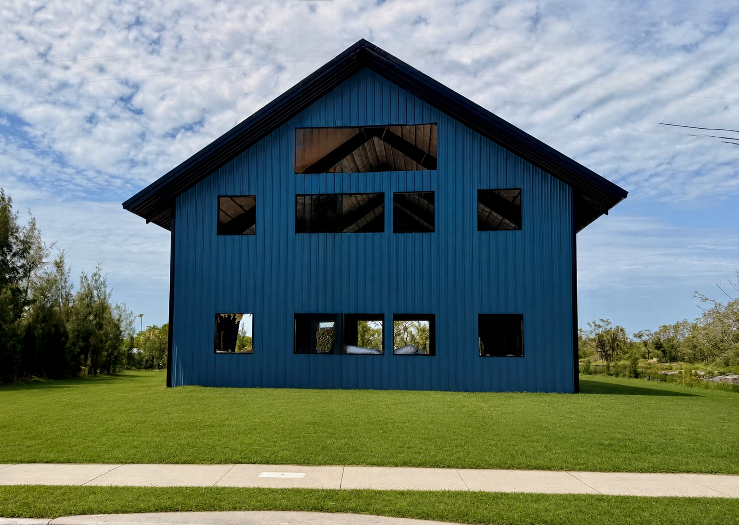 Blue barn-like house with large windows on a grassy field under a cloudy sky.
