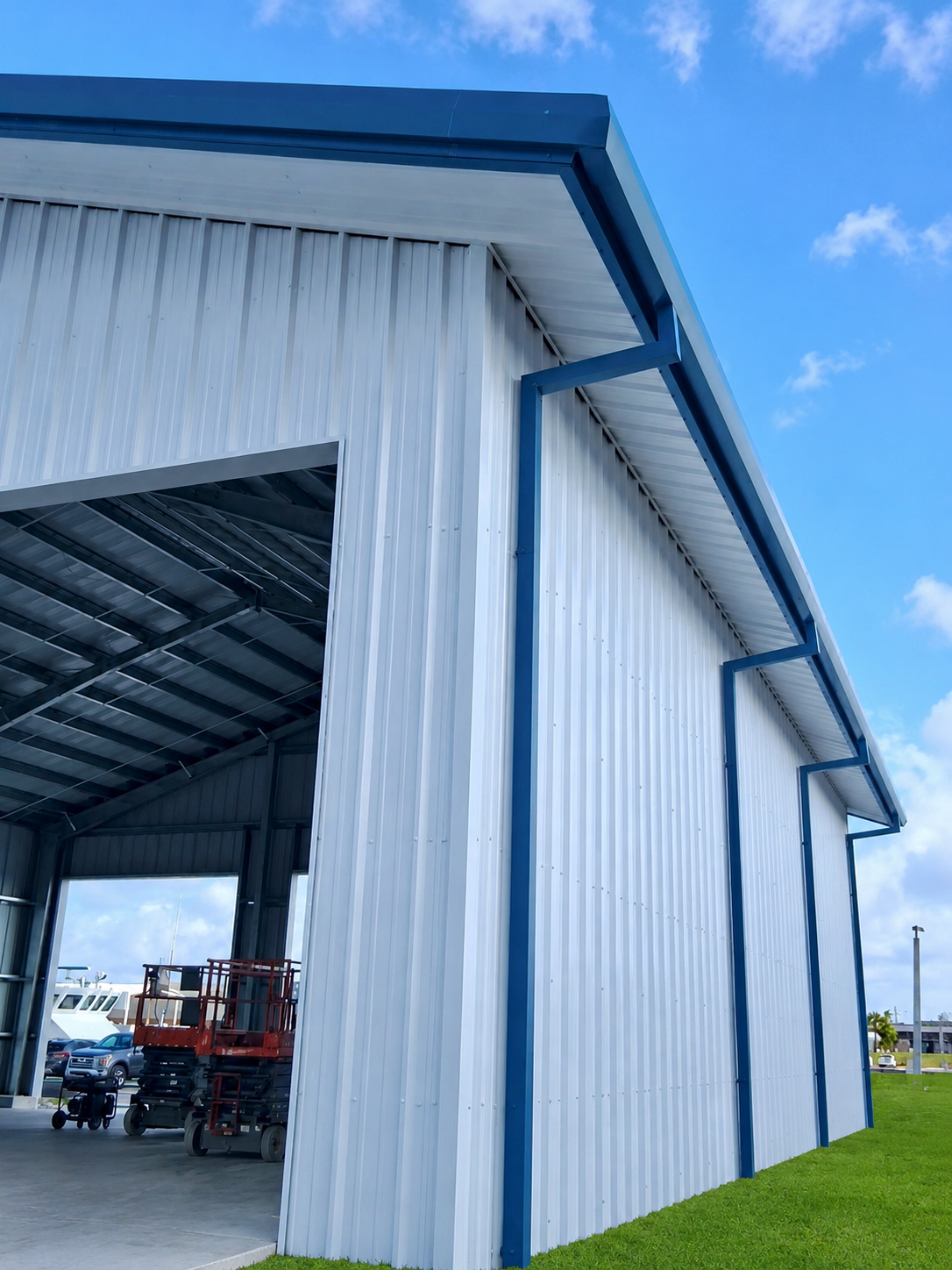 Blue-and-white metal barn with open doorway and vehicles inside, viewed from the outside on a grassy lot.