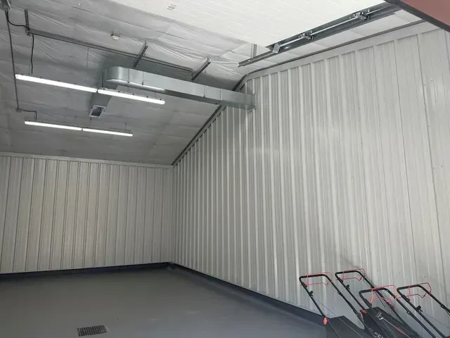 Empty metal-walled room with gray floor and exposed ceiling lights, with carts in the corner.