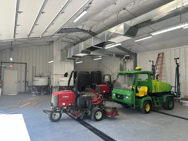 Workshop with a red cart and mower beside a green utility vehicle inside a metal garage.
