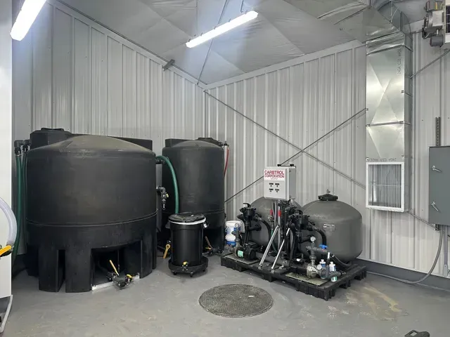 Industrial room with large black tanks, pumps, and pipes against corrugated metal walls.
