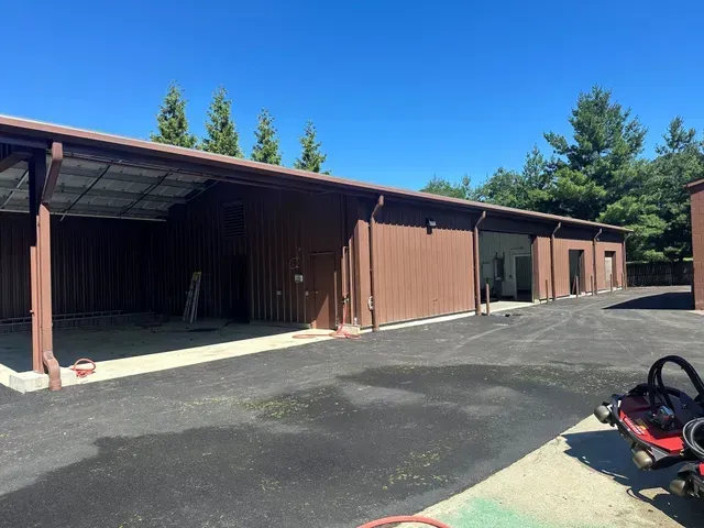 Brown storage buildings with open bays beside a paved lot under a clear blue sky.