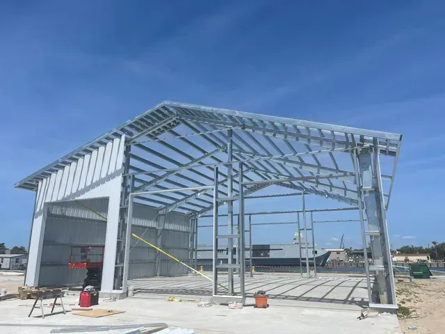Partially built steel-framed warehouse under a blue sky, with white wall panels and concrete slab.