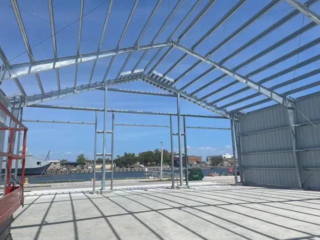 Steel-framed warehouse under construction with open walls and concrete floor in bright daylight.