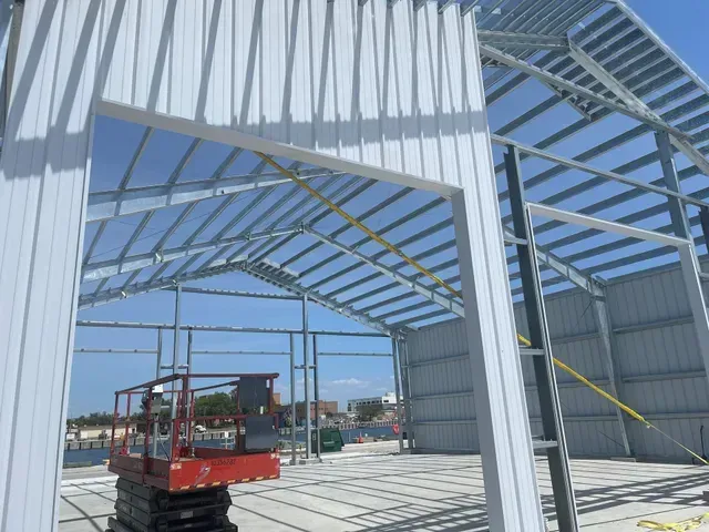 Steel-framed building under construction with a red scissor lift inside.