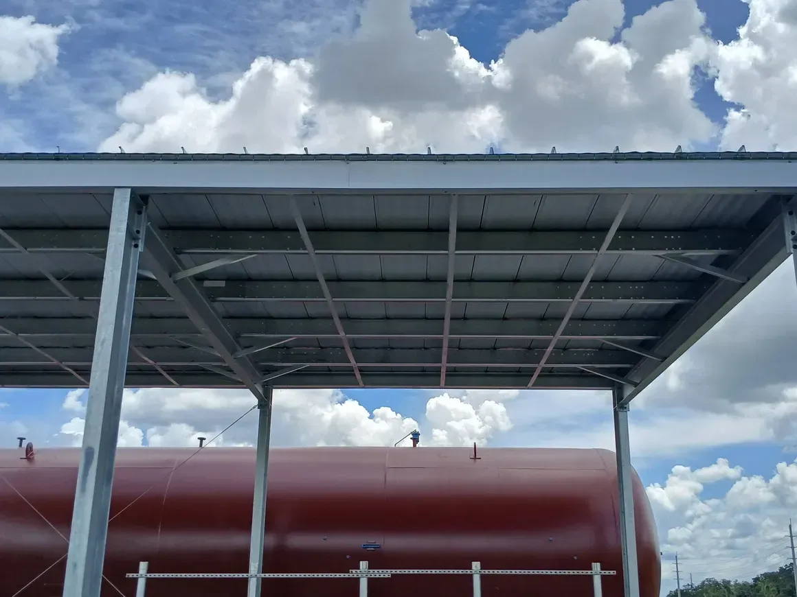 Metal roof canopy over a red tank beneath a cloudy blue sky