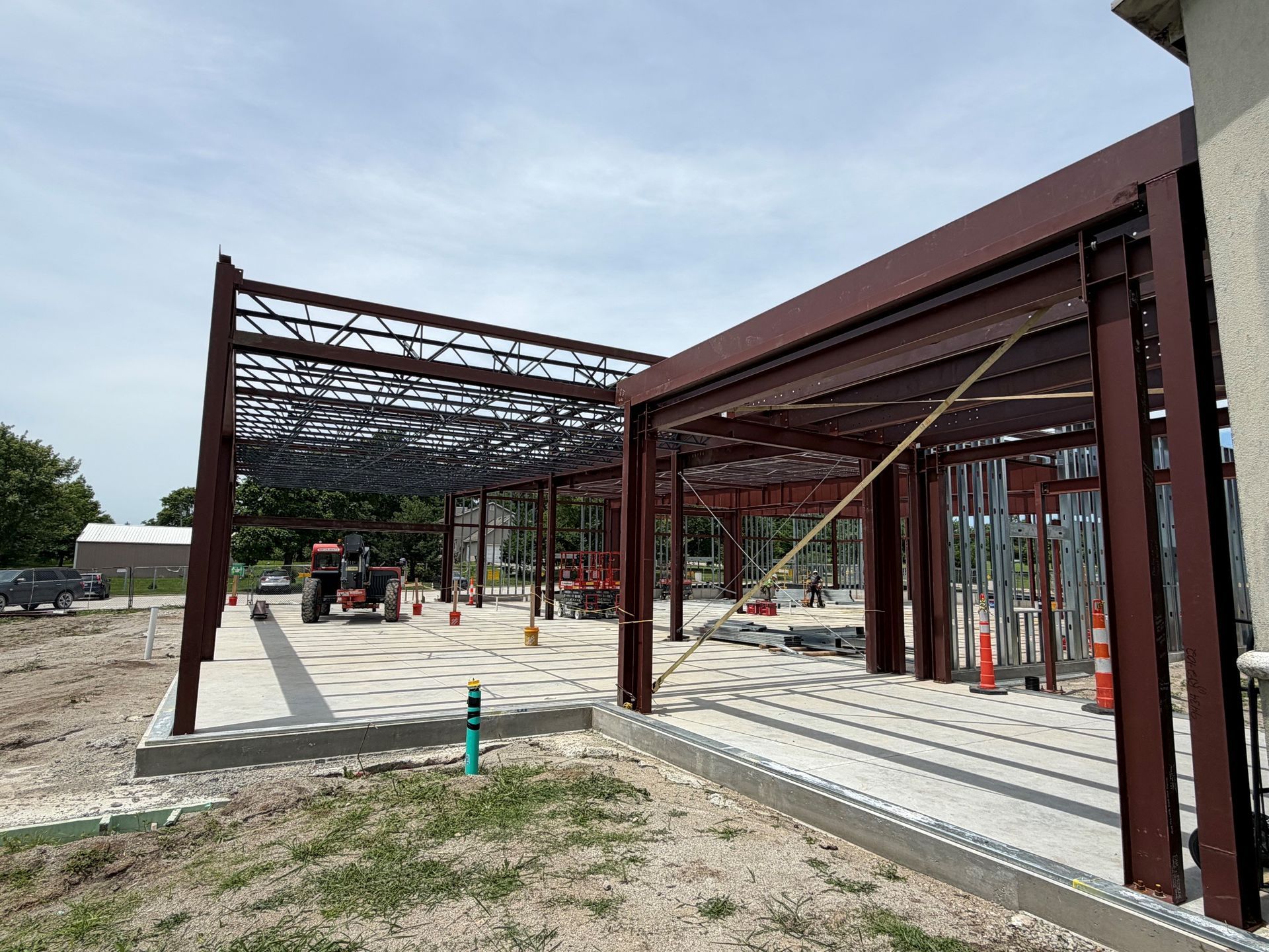 Steel building frame under construction on a concrete slab, with exposed red beams and open sky.