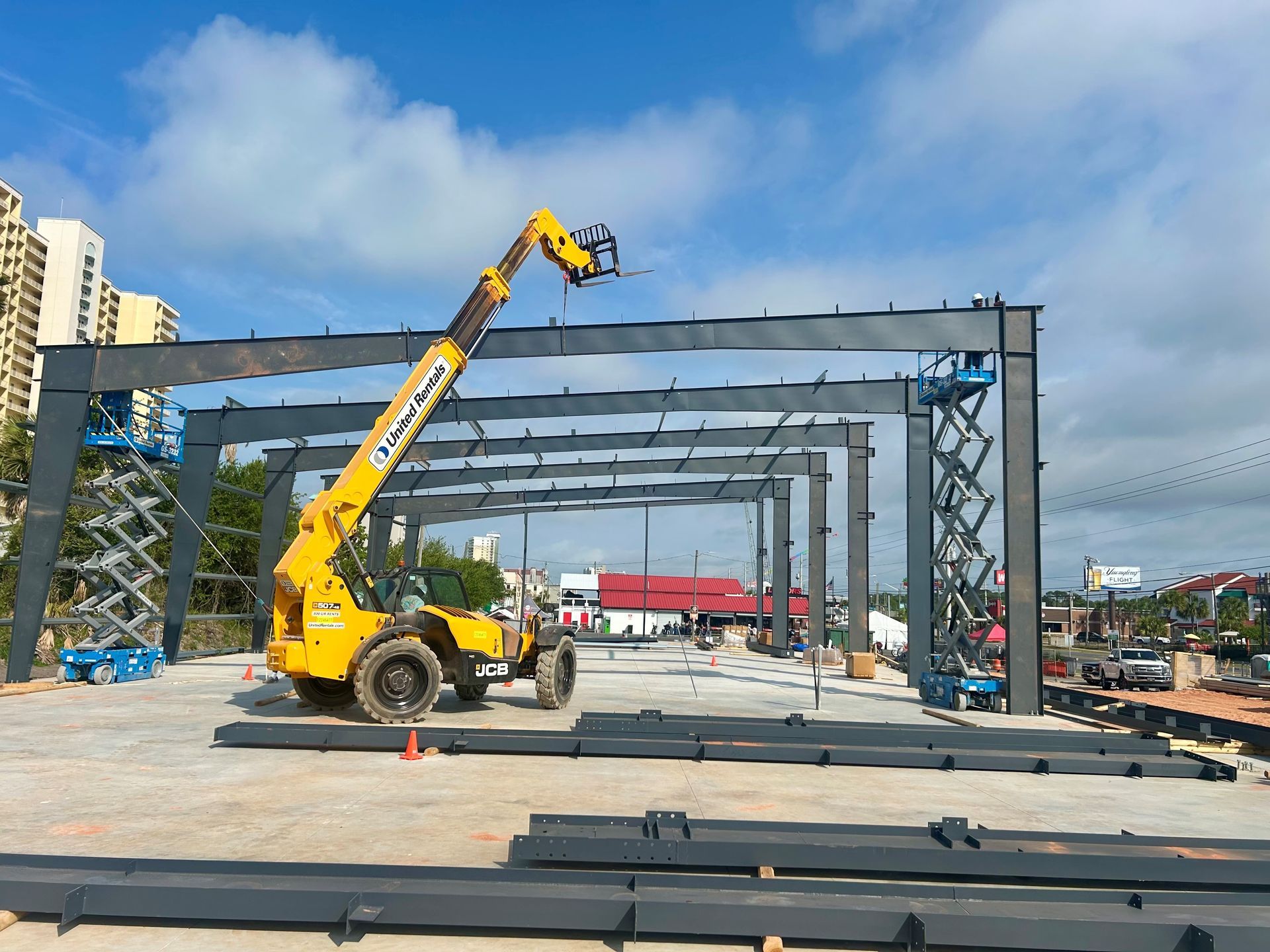 Yellow crane lifting steel beams at an outdoor construction site under a blue sky