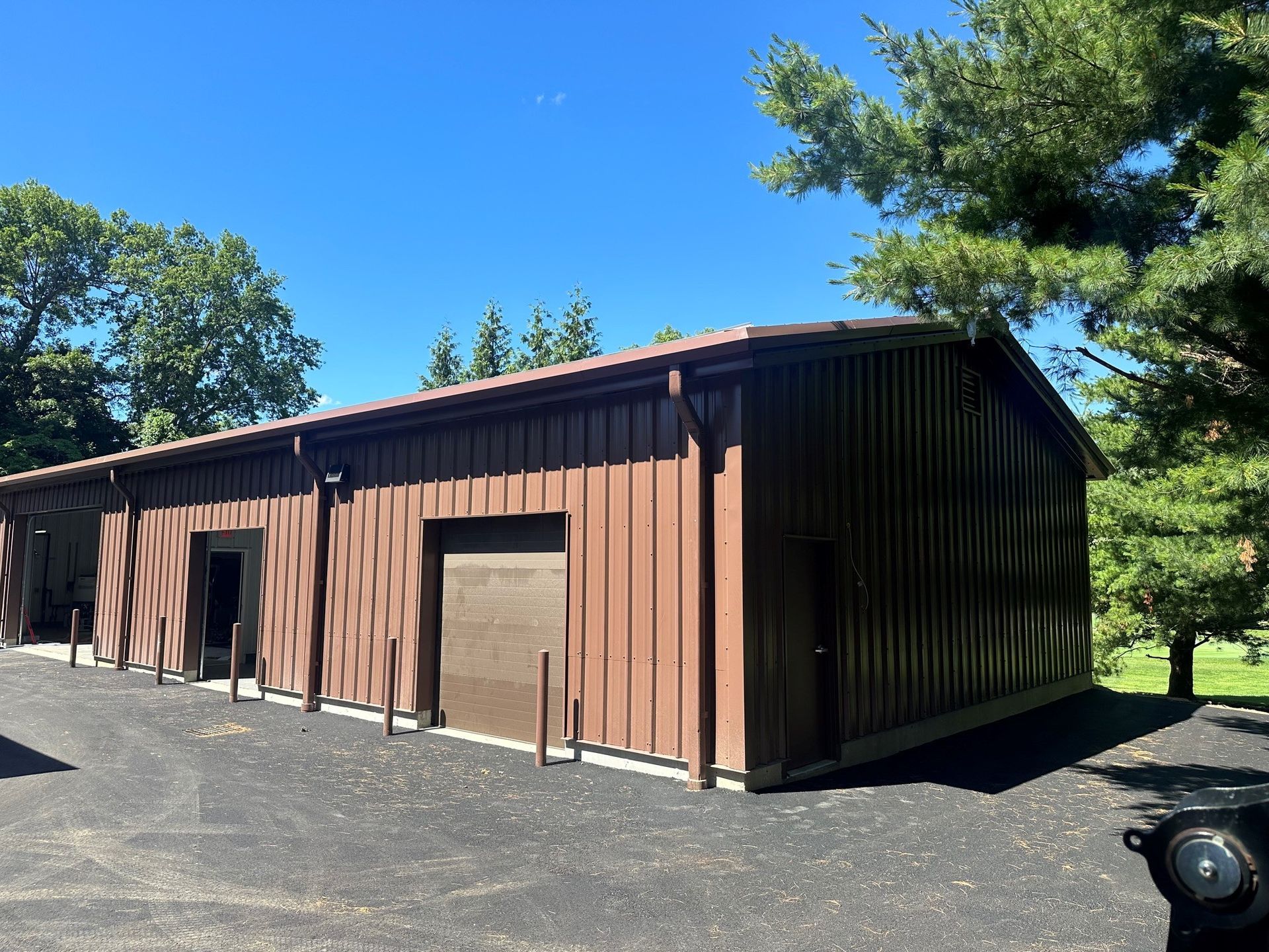 Brown metal garage with three doors beside a grassy yard under a blue sky