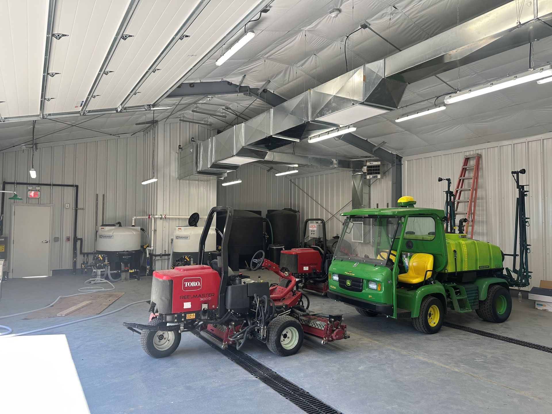 Indoor garage with a red utility vehicle and a green tractor parked under bright lights