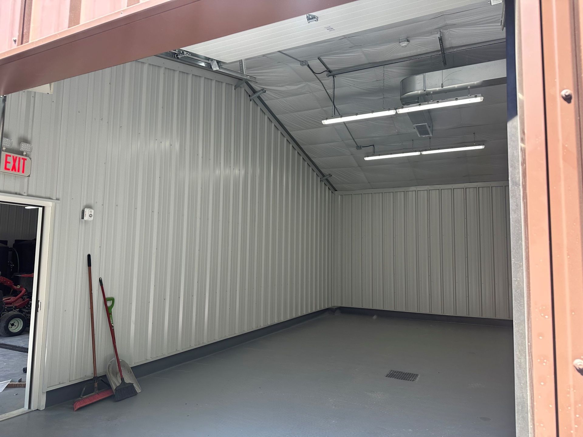 Empty garage bay with gray corrugated walls, concrete floor, and a broom by the left door.
