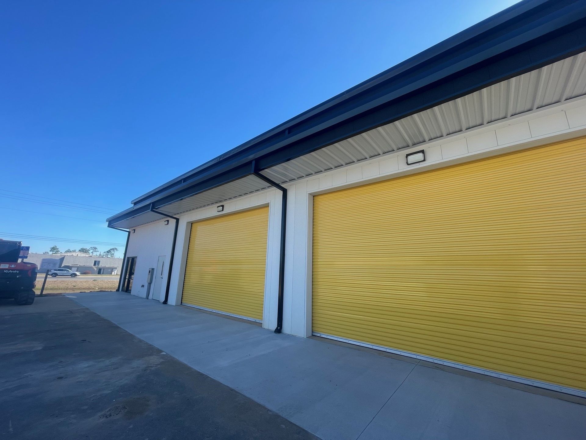 Long row of yellow storage unit doors along a sunny concrete walkway under a blue roofline