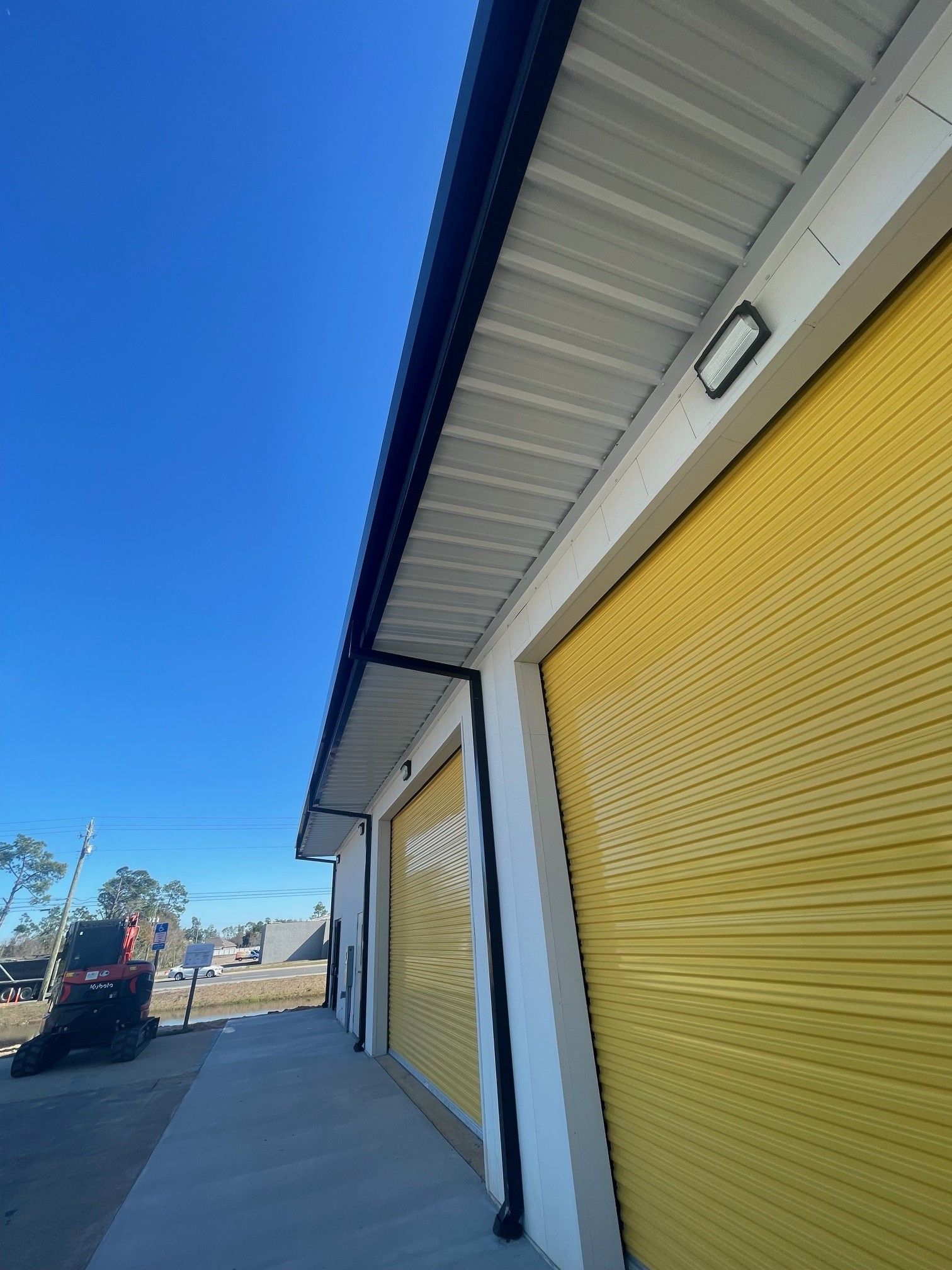 Industrial building with yellow roll-up doors and a covered walkway under a blue sky
