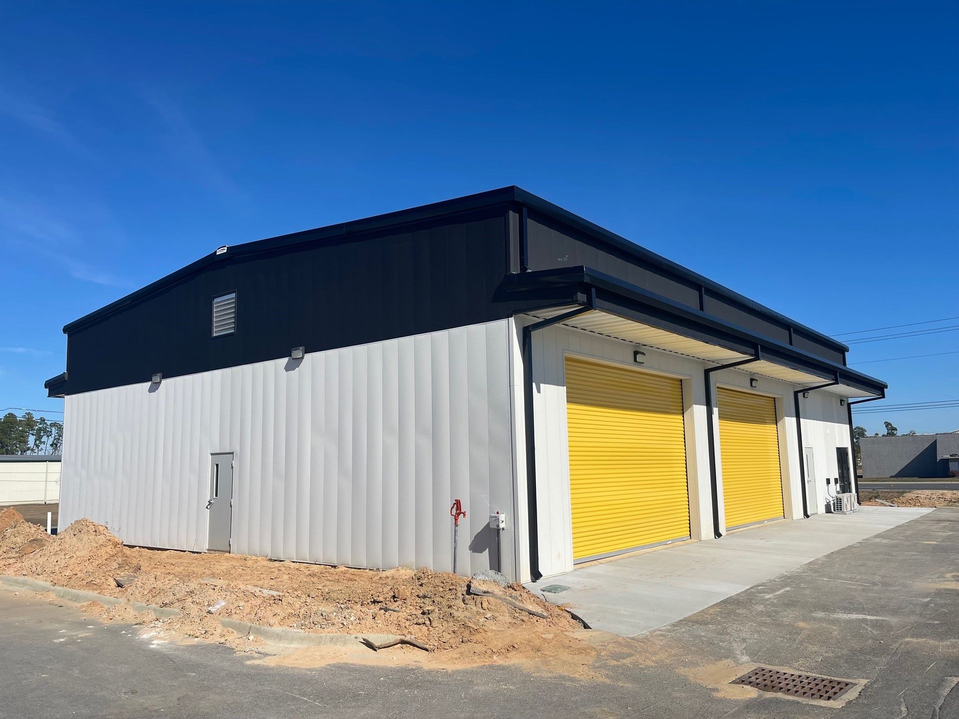 Industrial building with gray siding, black roof, and yellow garage doors on a gravel lot.