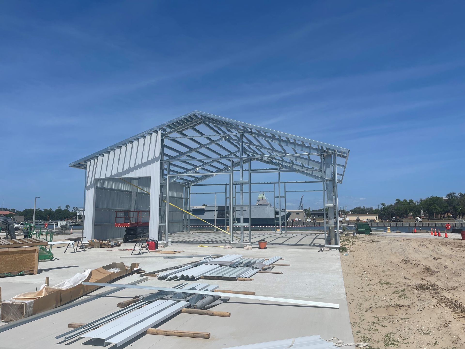 Partially built steel warehouse frame on a construction site under a blue sky