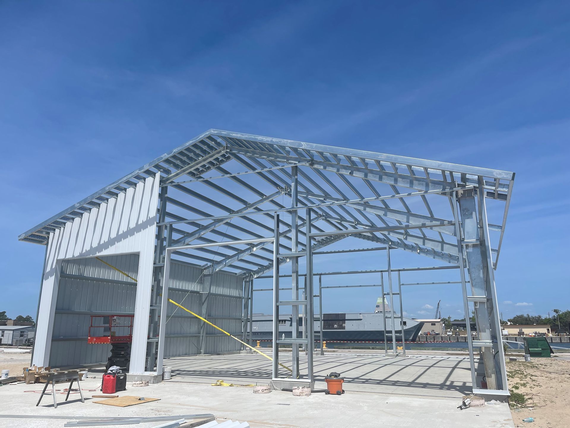 Steel-framed warehouse under construction on a sunny day, with scaffolding and a partly finished roof.