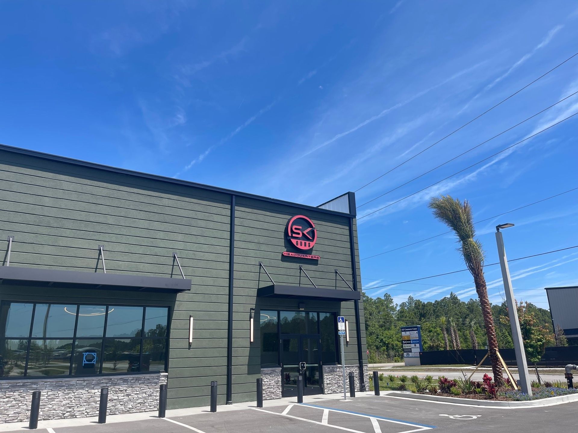Exterior of a modern restaurant with dark green siding, large windows, and a round red sign under a blue sky.