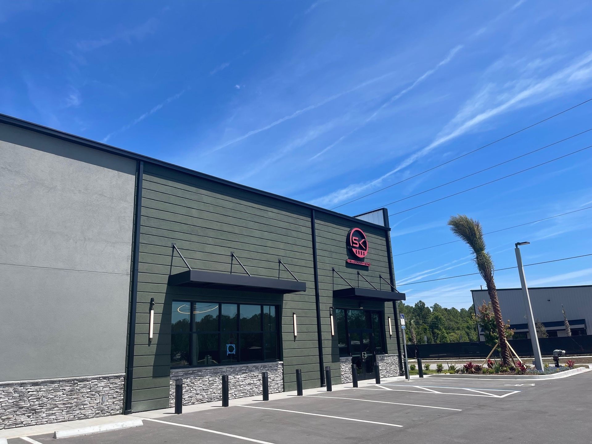 Exterior of a modern store with a parking lot, blue sky, and a palm tree nearby