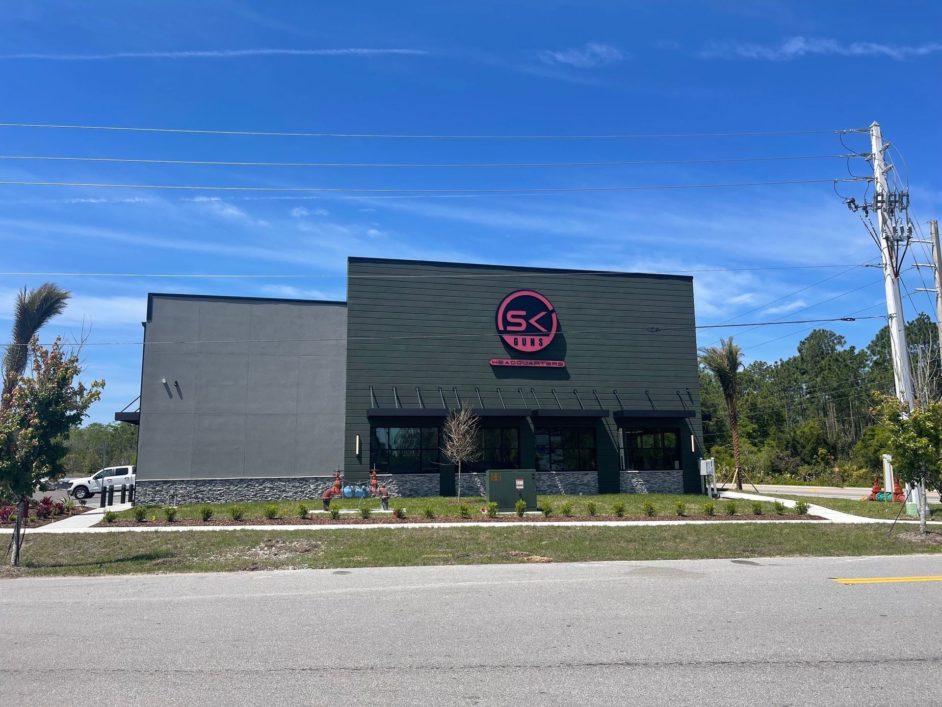 Modern commercial building with a black-and-pink circular logo, landscaped frontage, and blue sky