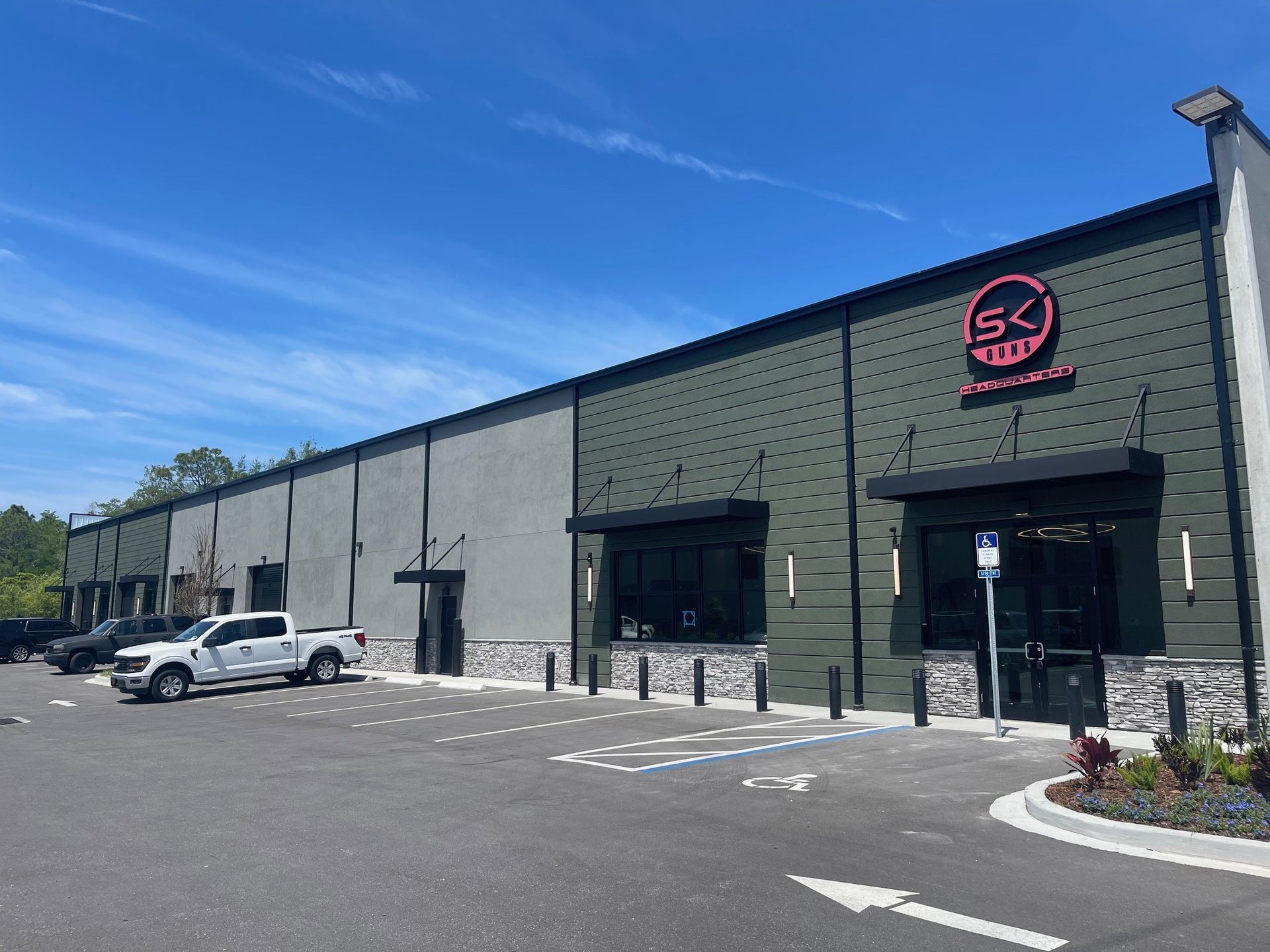 Long gray commercial building with black trim, parked white van, and pink circular logo by the entrance