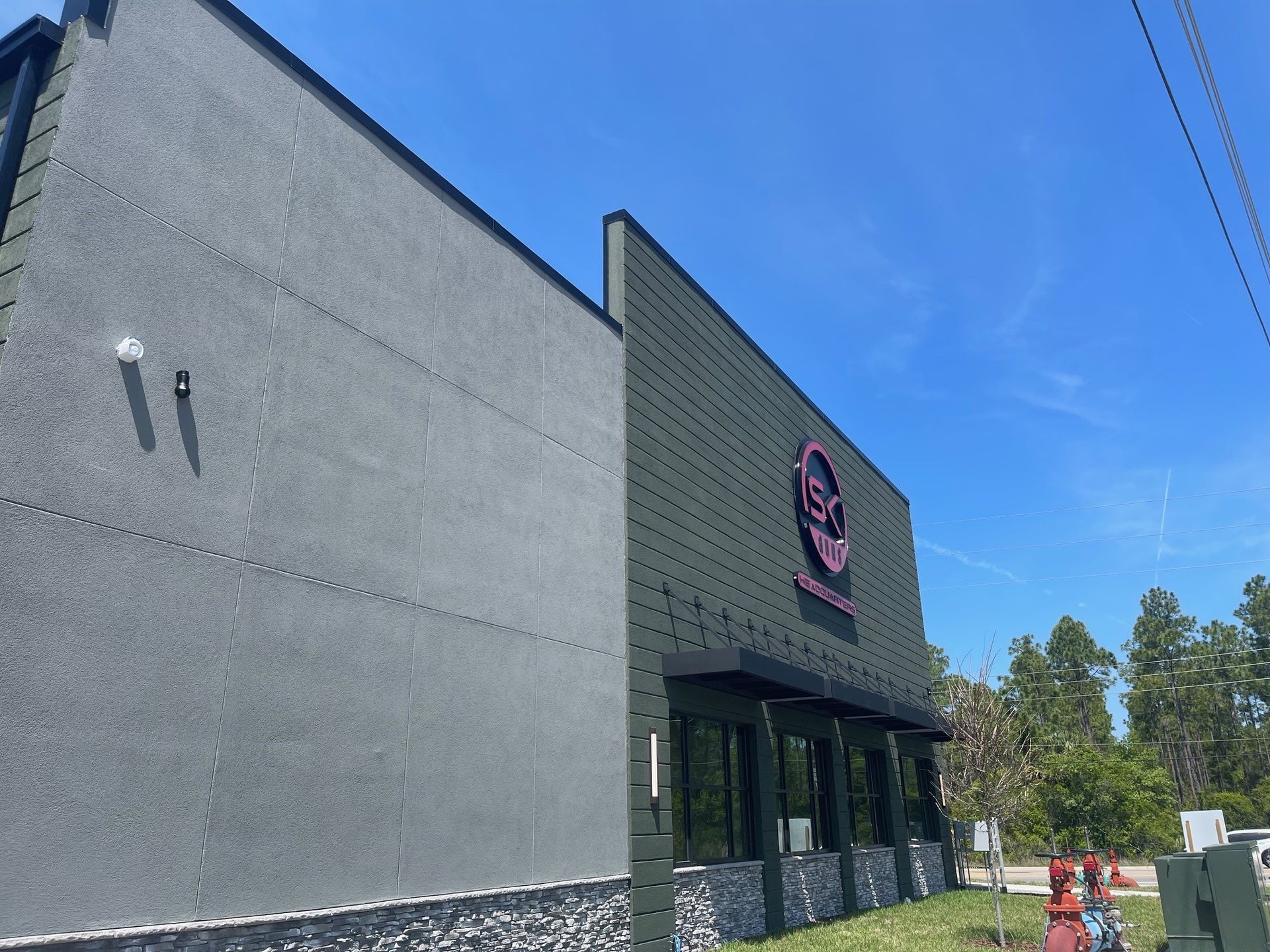Exterior of a modern gray storefront with a pink sign, stone base, and blue sky overhead