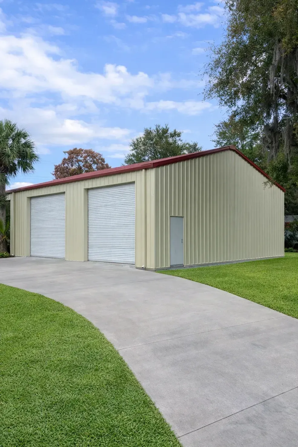 Beige metal garage with two white roll-up doors beside a curved concrete driveway.
