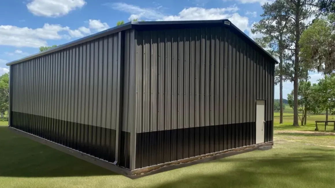 Black metal barn-like building on a grassy field under a blue sky